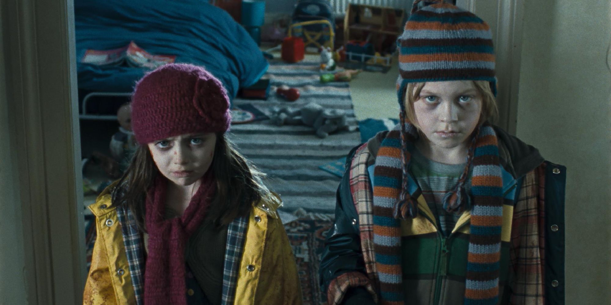 Two children stand in front of a messy bedroom, covered in scuffs.