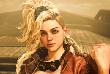 Monster Hunter Wilds trailer screenshot showing a young woman with long blonde hair tied back into a ponytail smiling slightly, pumping her left fist in the air