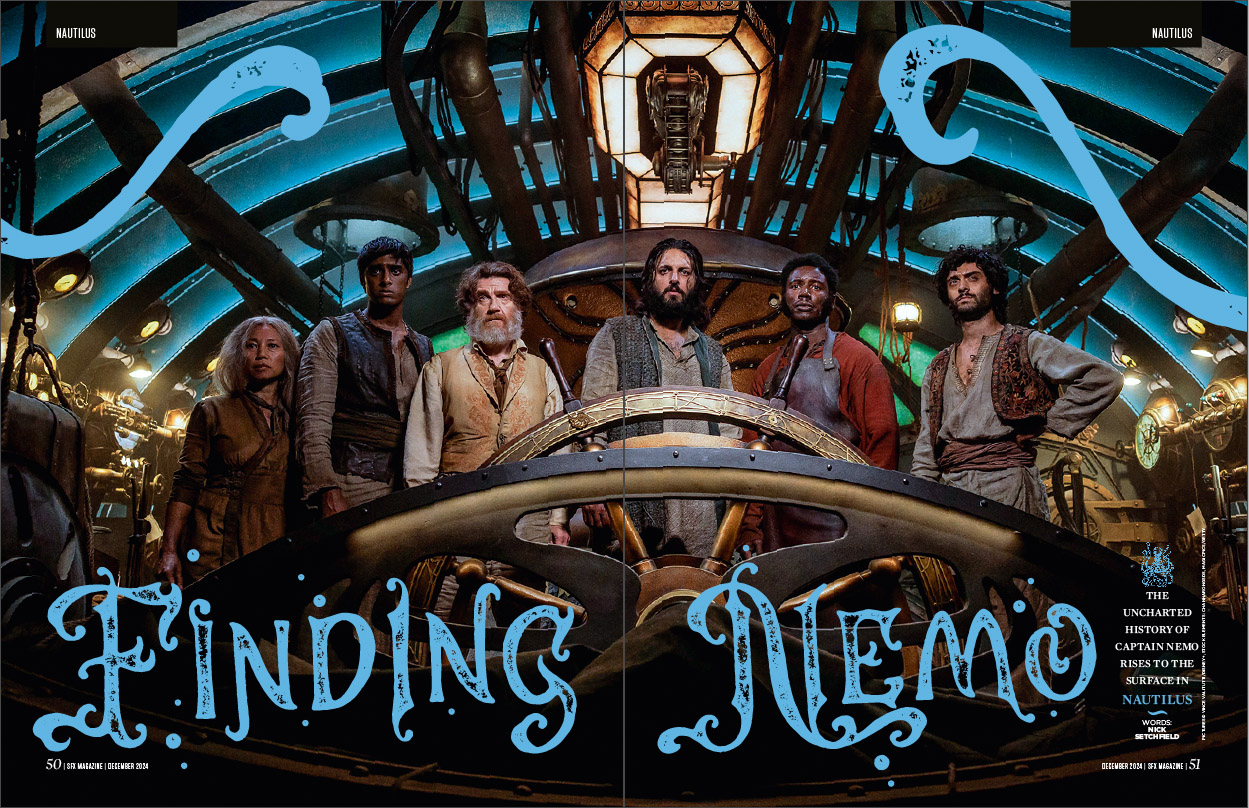 Six of the cast of Nautilus standing behind the helm of the sub.