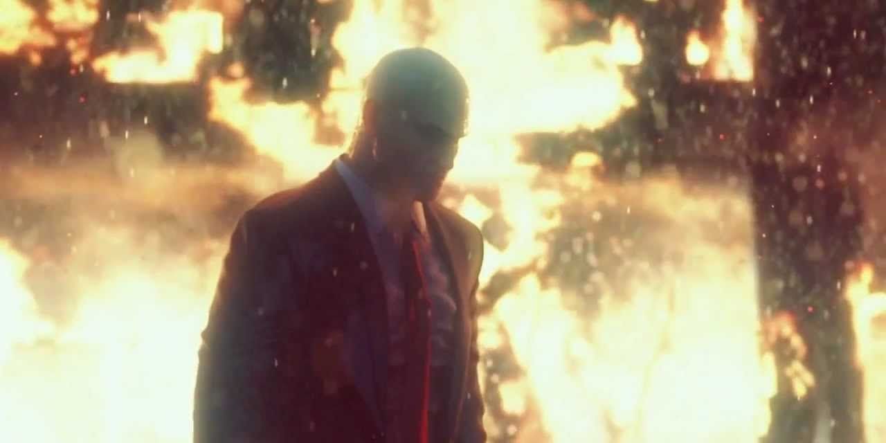 Agent 47 in the rain with fire burning behind him in Hitman: Absolution.