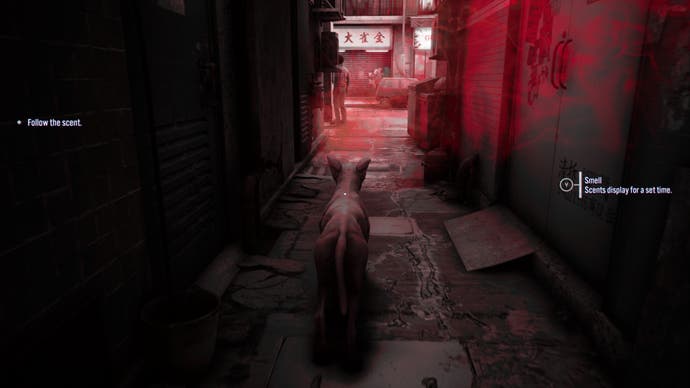 A screenshot from Slitterhead showing a stray dog in the shadows of an alleyway. A stylised red mist wafts in from the main street, which the dog is encouraged to follow. The on-screen text says: 