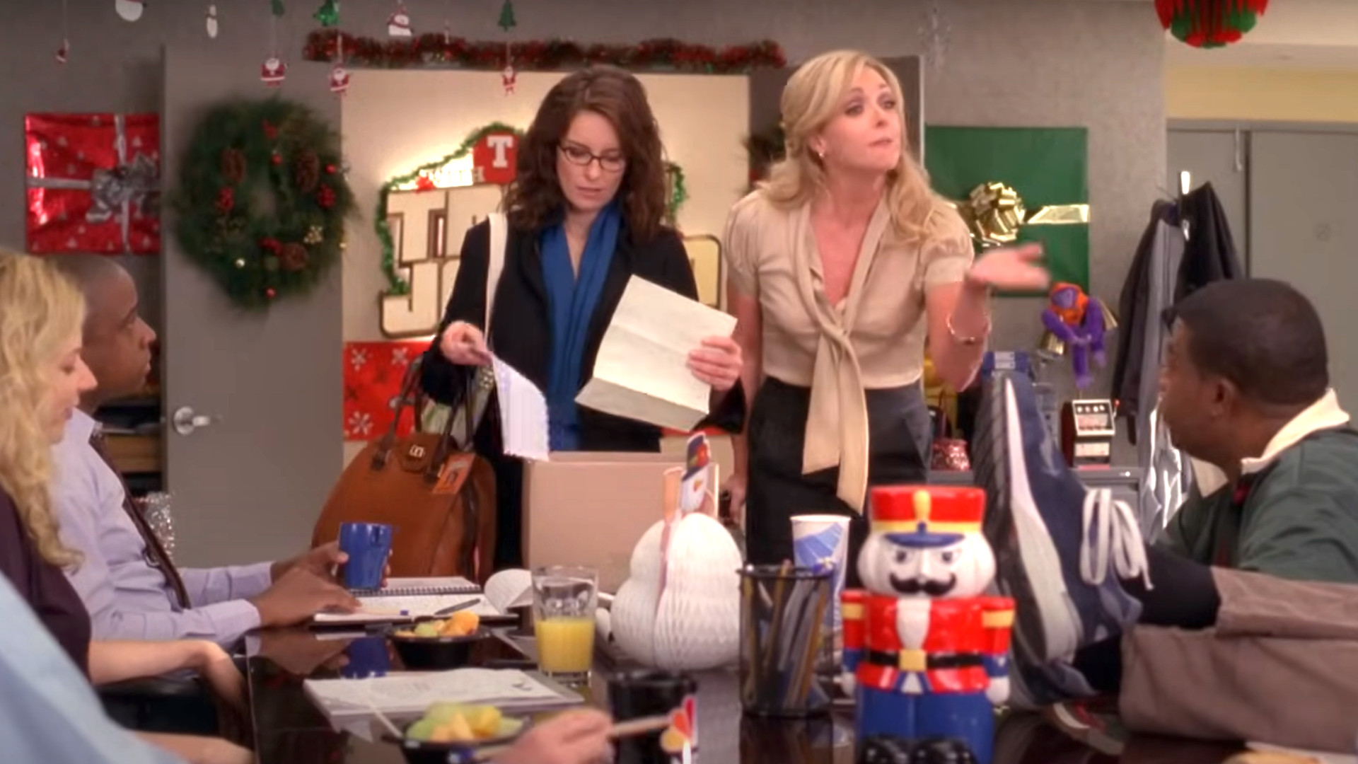 Tina Fey as Liz Lemon and Jane Krakowski as Jenna Maroney talking to a table full of people during one of the best shows on Hulu, 30 Rock.