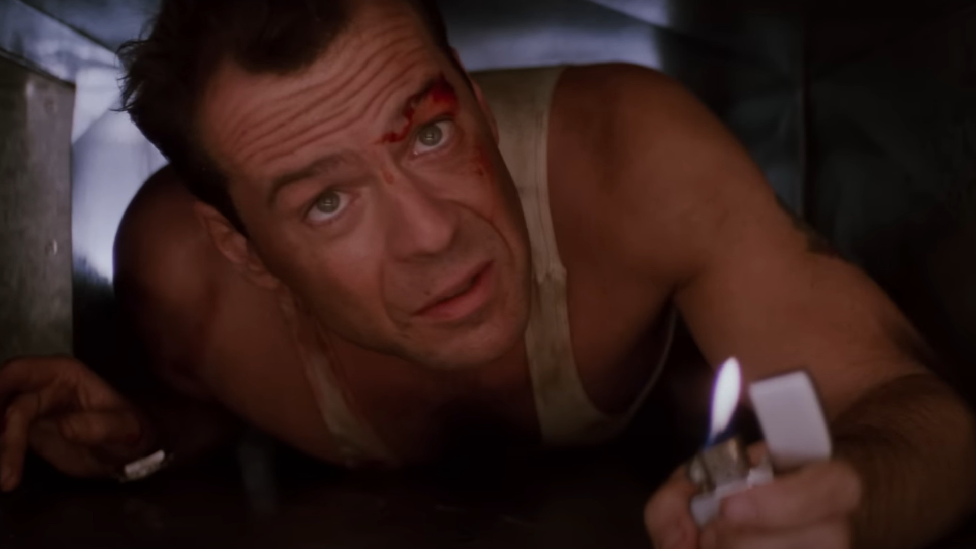 Bruce Willis as John McClane holding up a lighter while crawling through a vent during one of the best movies on Hulu, Die Hard.