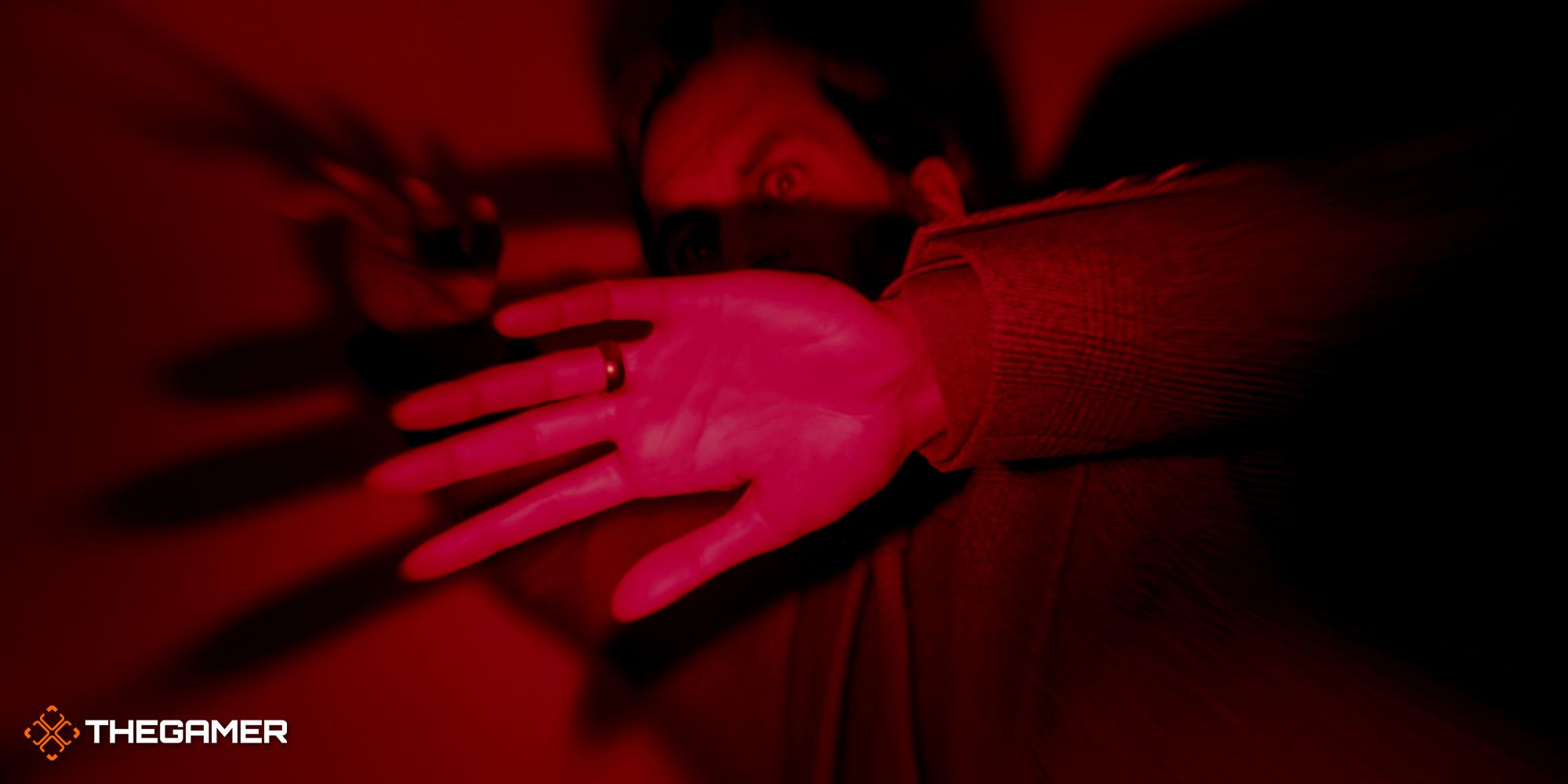 Alan in red lighting in the studio putting his arms in front of his face in fright of the Dark Presence.