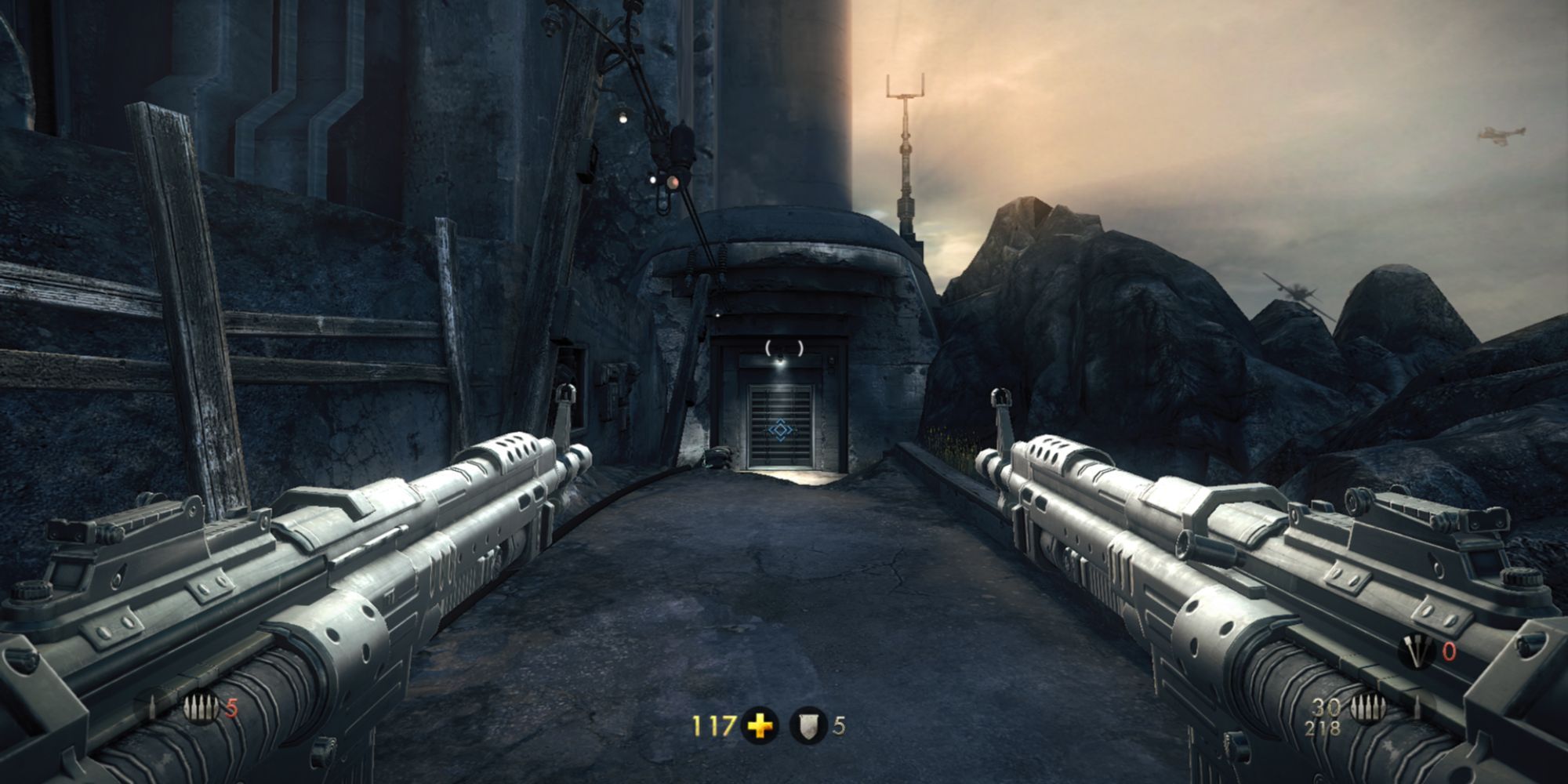 A screenshot from Wolfenstein: The New Order, wherein the player is dual-wielding assault rifles and heading towards a bunker.