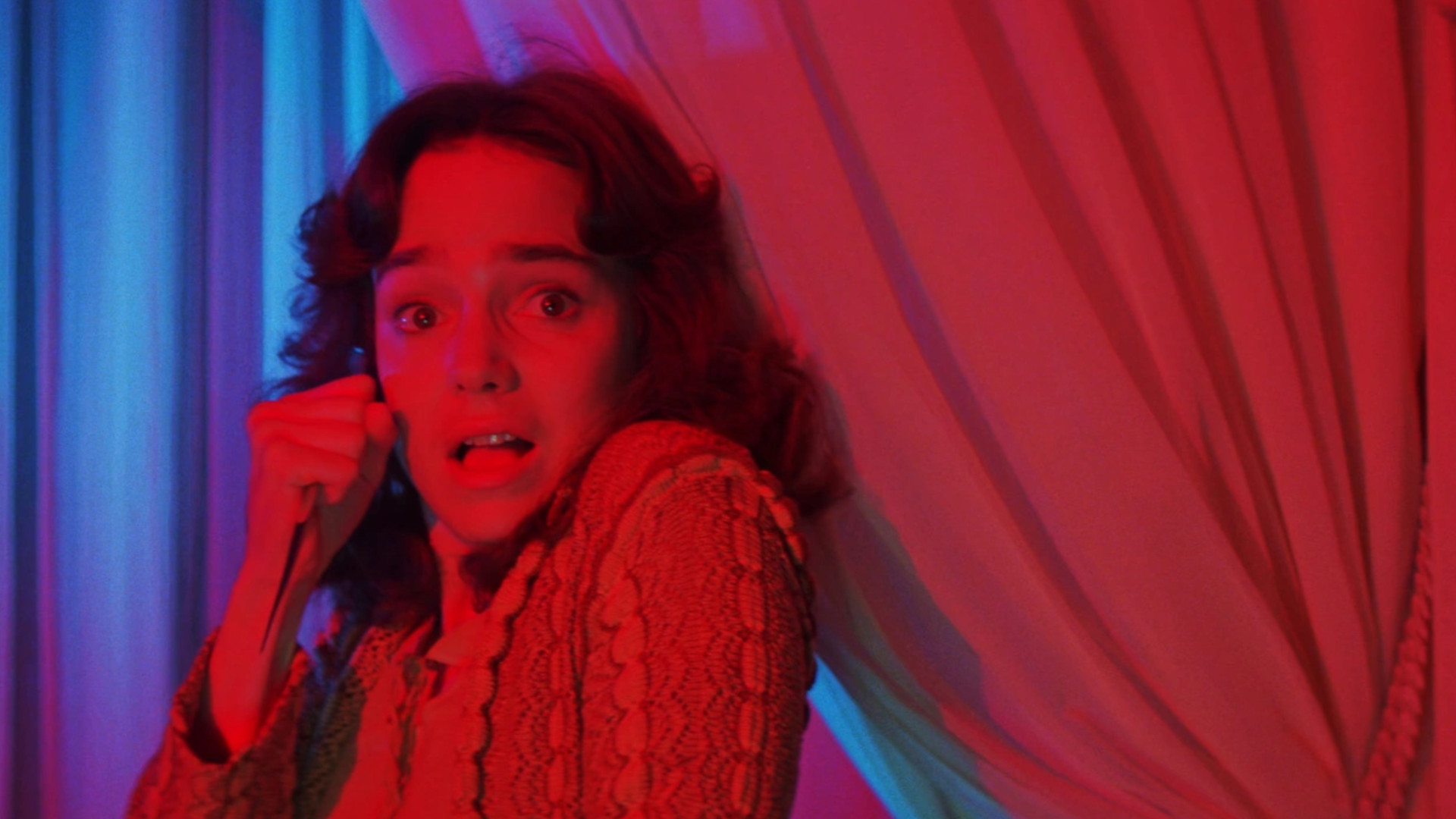 Jessica Harper as Suzy Bannion holding a knife in a room with red lighting during the horror movie, Suspiria.