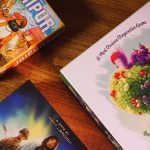 Jaipur, Pandemic, and Paint the Roses boxes on a wooden table, seen from above