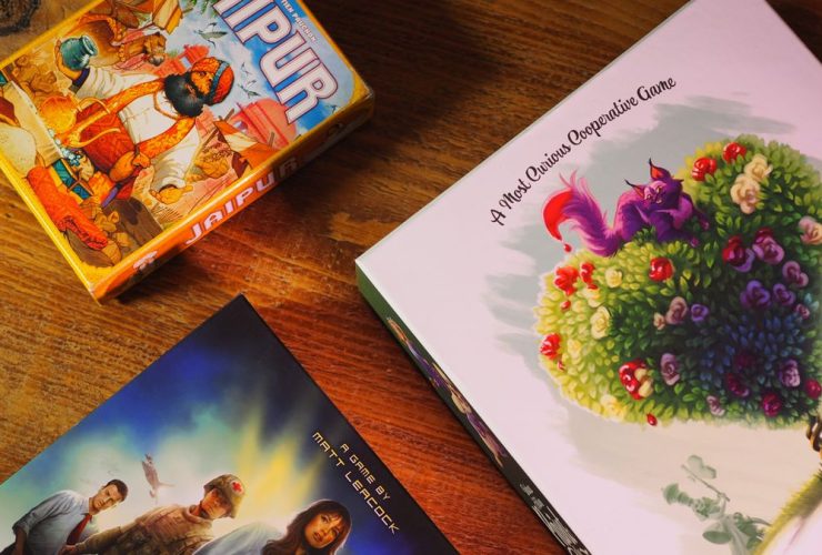 Jaipur, Pandemic, and Paint the Roses boxes on a wooden table, seen from above