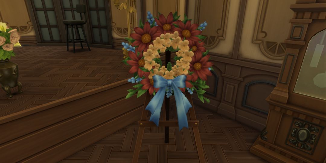 A memorial wreath made out of orange and red flowers stands in a room, finished with a blue bow.