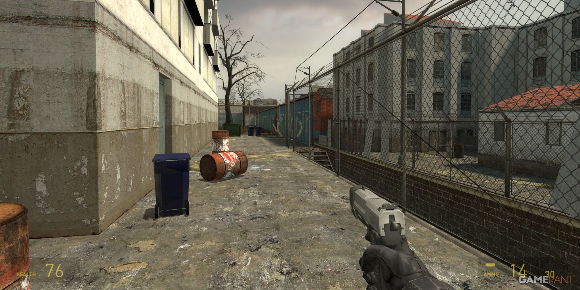 Urban outdoor area with barrels and fences, player holding a pistol in Half-Life 2