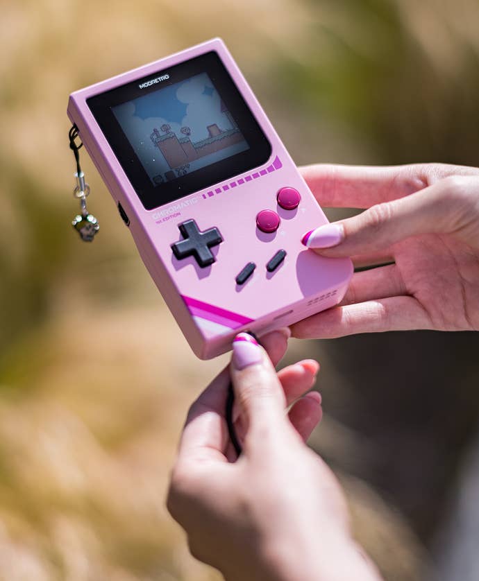 A bubblegum pink Chromatic handheld, with a small charm hanging off it.