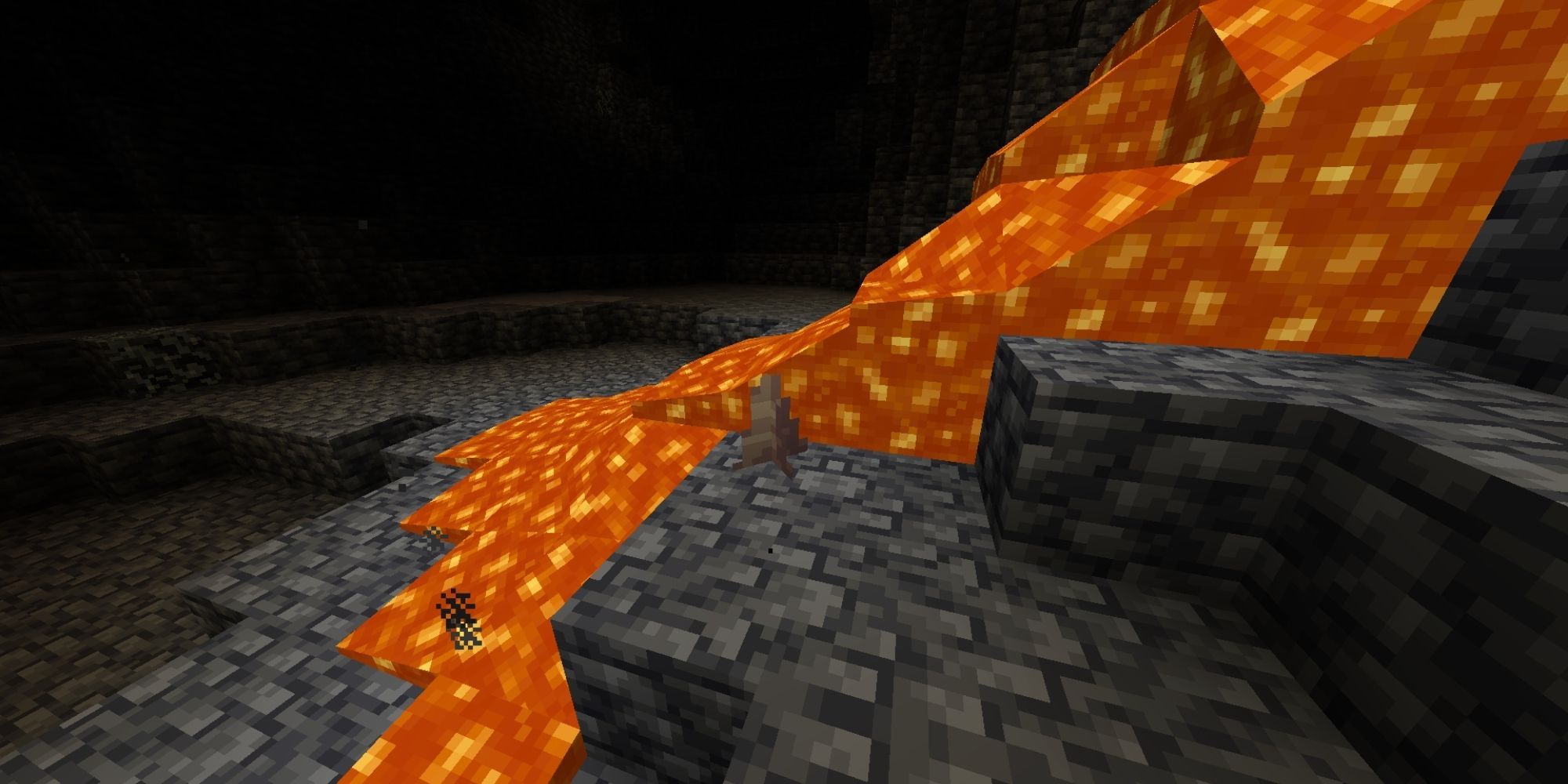 A small stalagmite seen near a hot stream of lava in a dark cave.