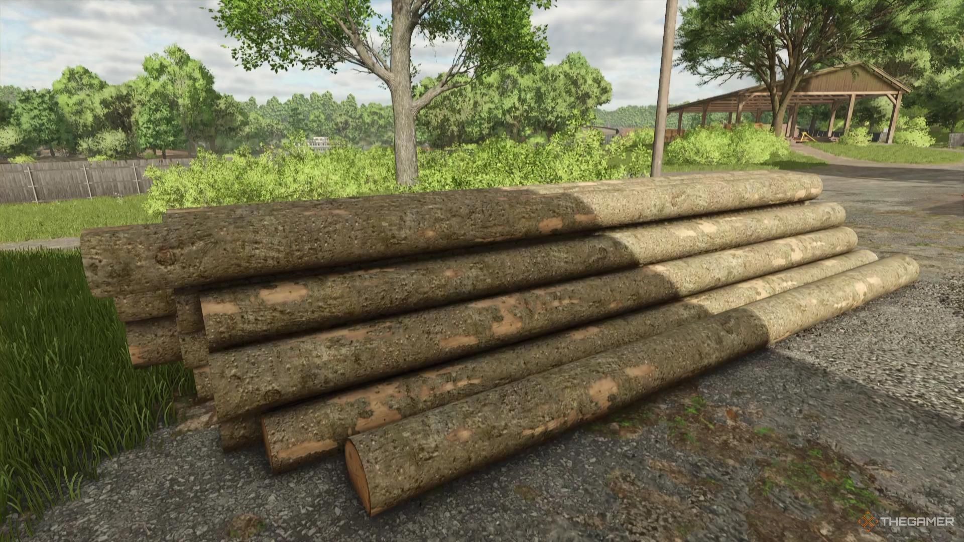 A group of logs sit stacked near a sawmill in Farming Simulator 25.