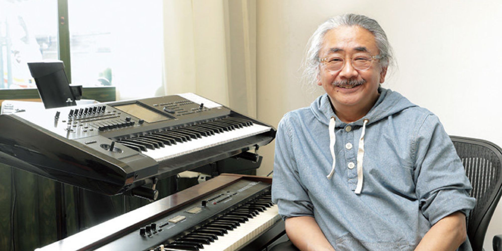 Final Fantasy composer Nobuo Uematsu smiles next to his keyboard setup