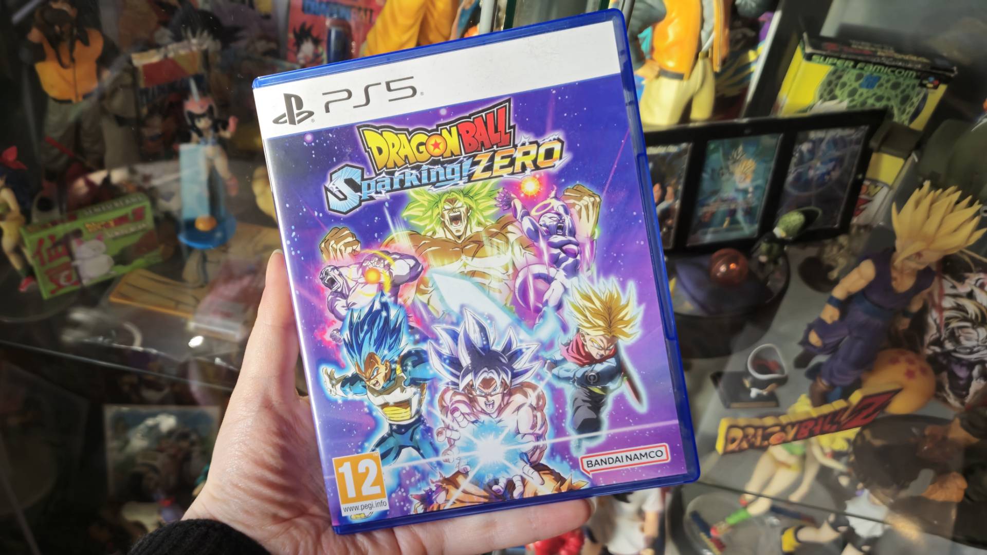 Image of author Rosalie Newcombe holding a copy of Dragon Ball Sparking Zero on the PS5 in their hand in front a lot of Dragon Ball merchandise.