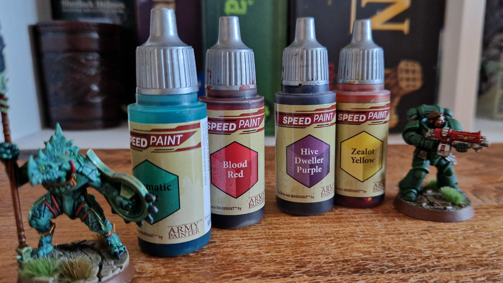 Speedpaint bottles on a wooden table beside two miniatures, a lizardman Saurus Warrior and a Space Marine