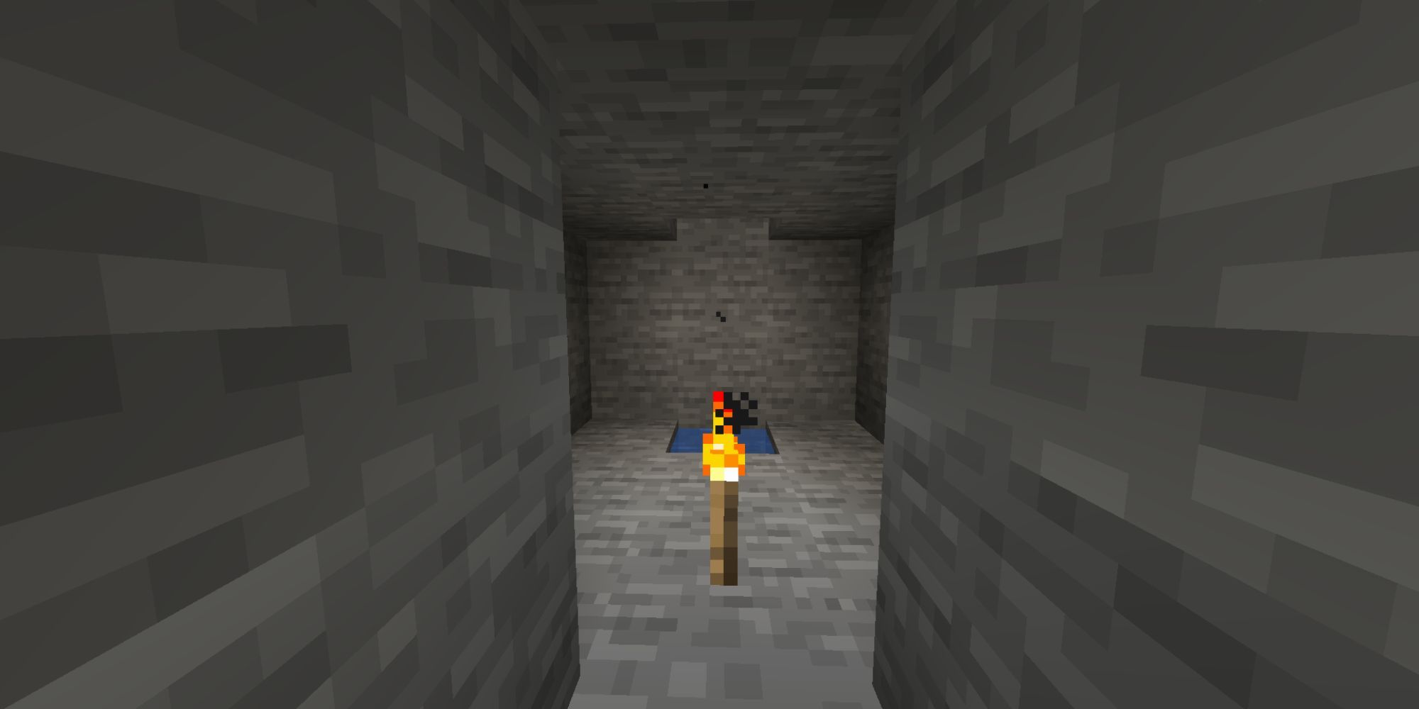 A small, stone room underground, with a torch and water inside.