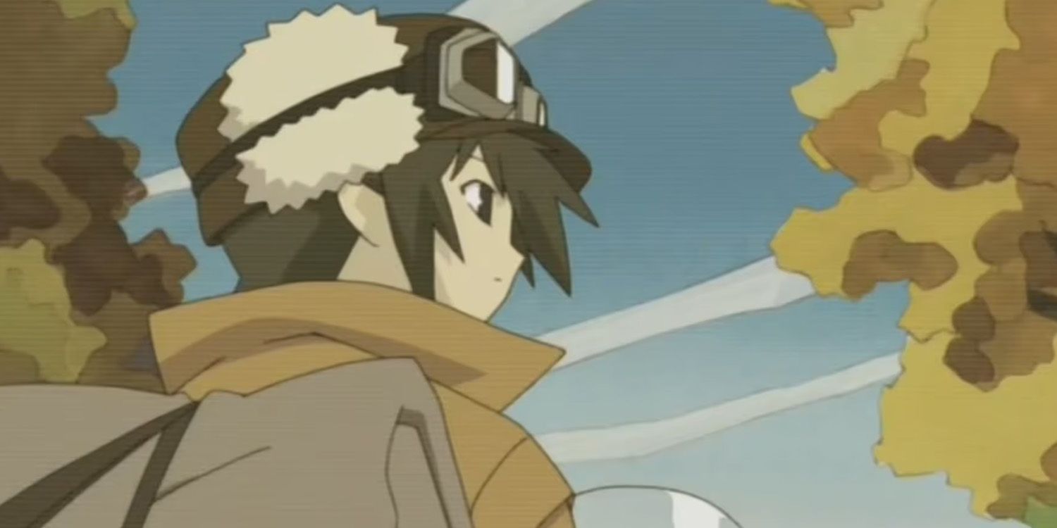 Kino looks at the horizon. Kino has short hair and a tan overcoat. A pair of aviator goggles is strapped to Kino's hat.