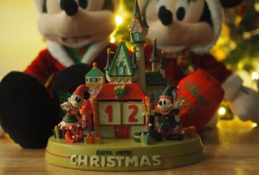 Disney Christmas Countdown Castle in front of a Mickey and Minnie Mouse plush set, with a twinkling tree in the background