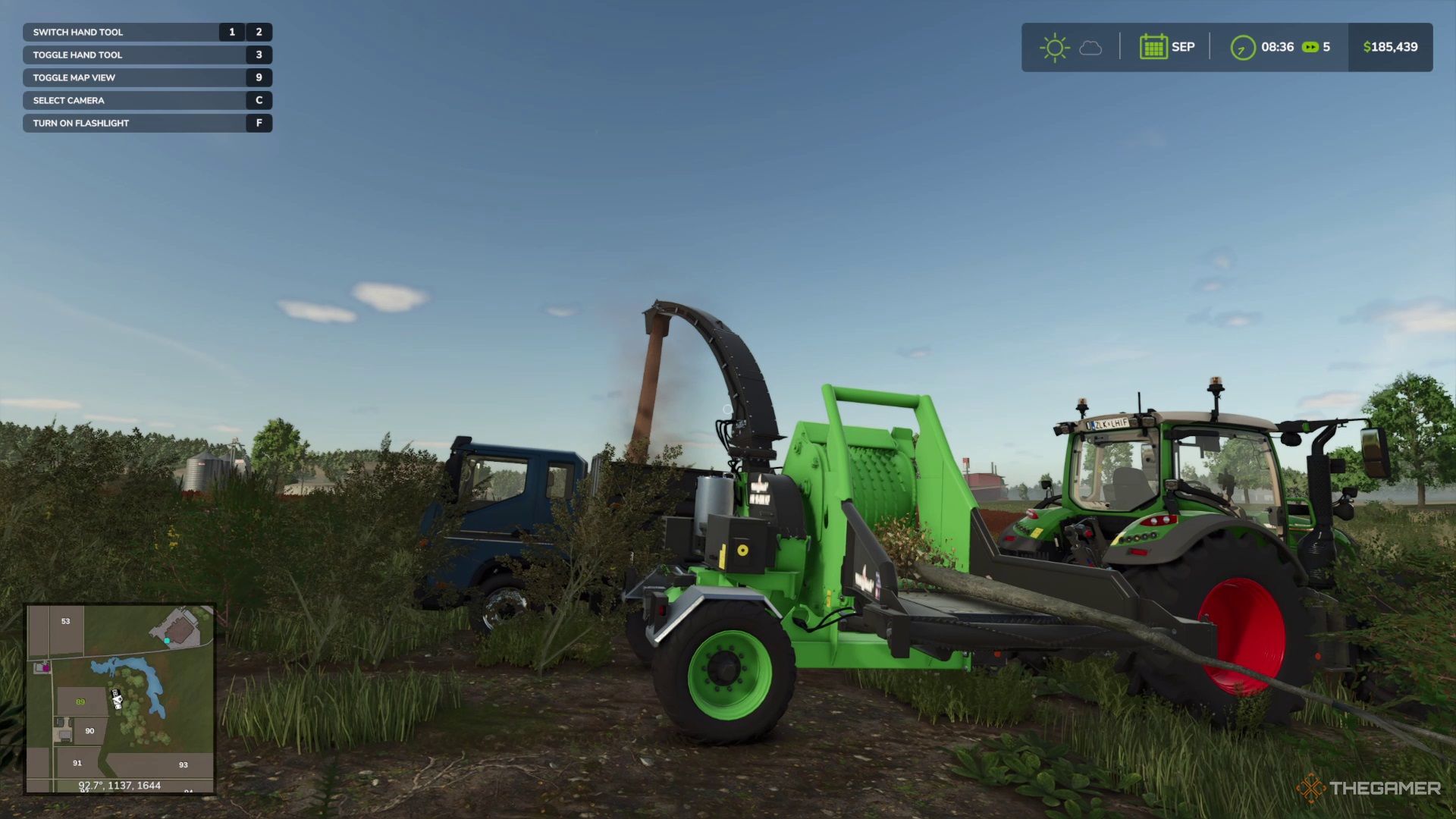 A Wood Chipper grinding a tree and chuting the chips into a trailer in Farming Simulator 25.