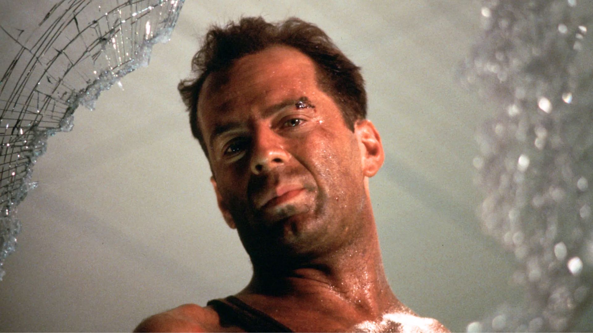 Bruce Willis as John McClane looking through a broken window during Die Hard.