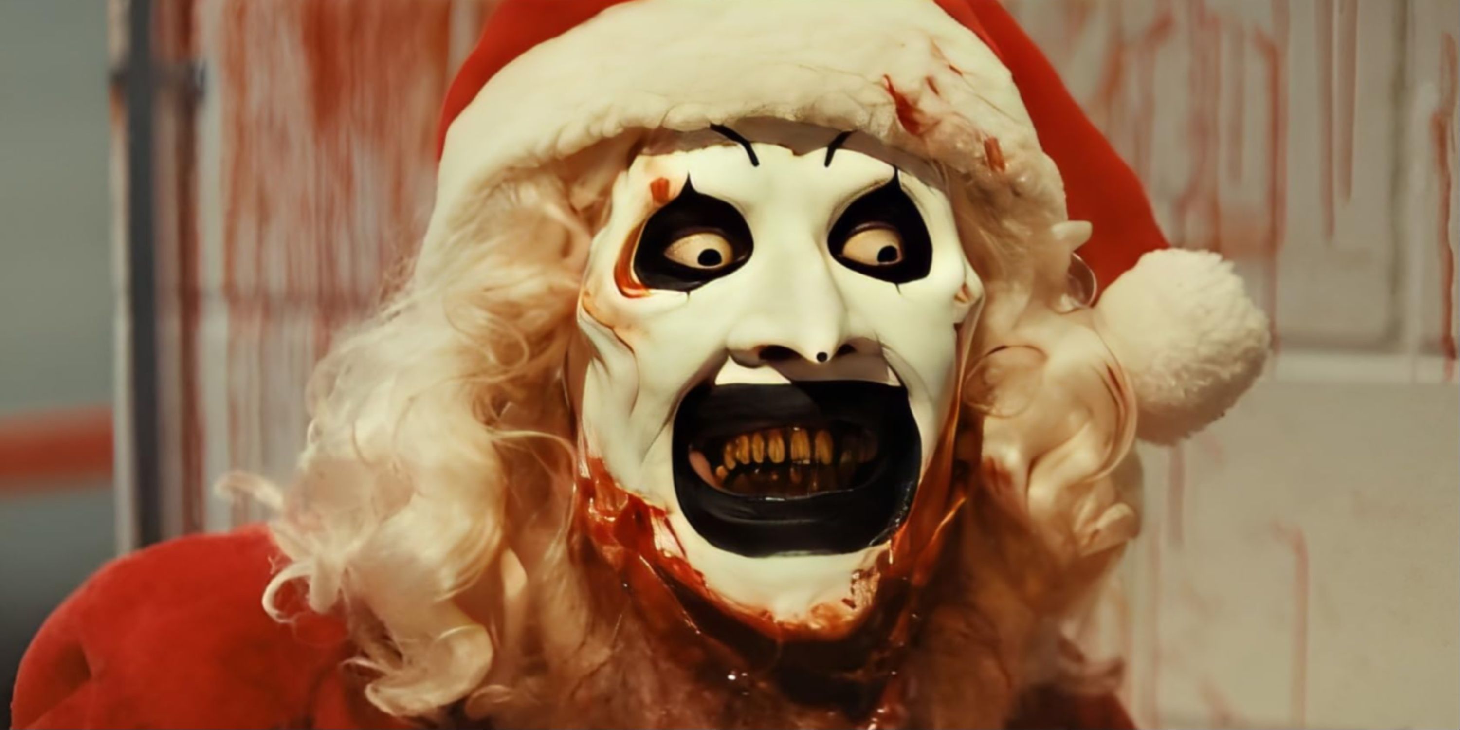 A close-up of Art the Clown's bloody face wearing a santa outfit during the chainsaw kill in the shower in Terrifier 3.