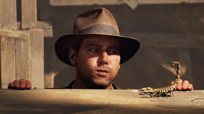 Indiana Jones blows air at a scorpion as he hangs from a ledge in Indiana Jones and the Great Circle.