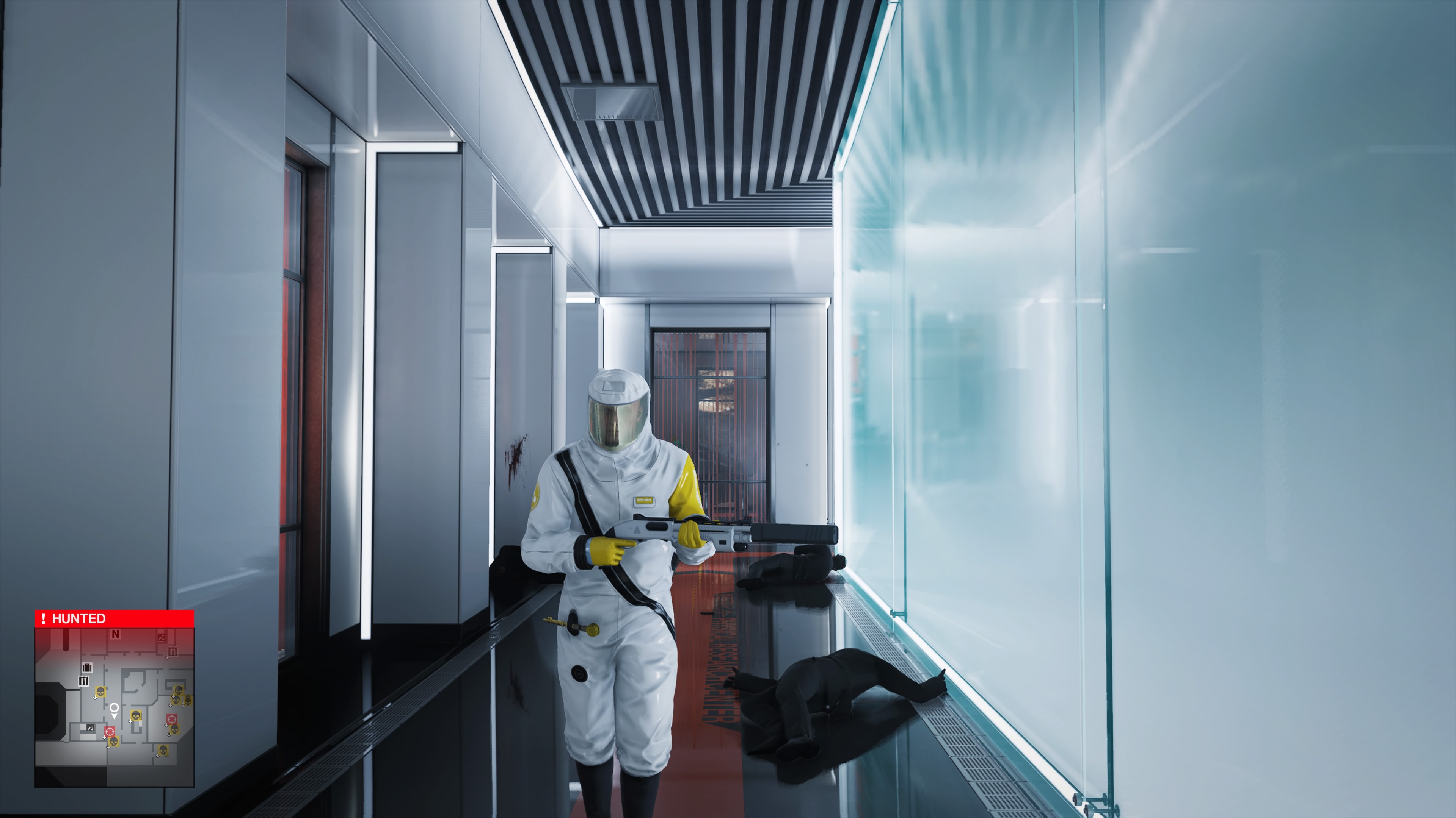 Walking through a corridor laden with bodies in a hazmat suit while playing the 2016 Hitman DLC mission Patient Zero in Hitman 3.