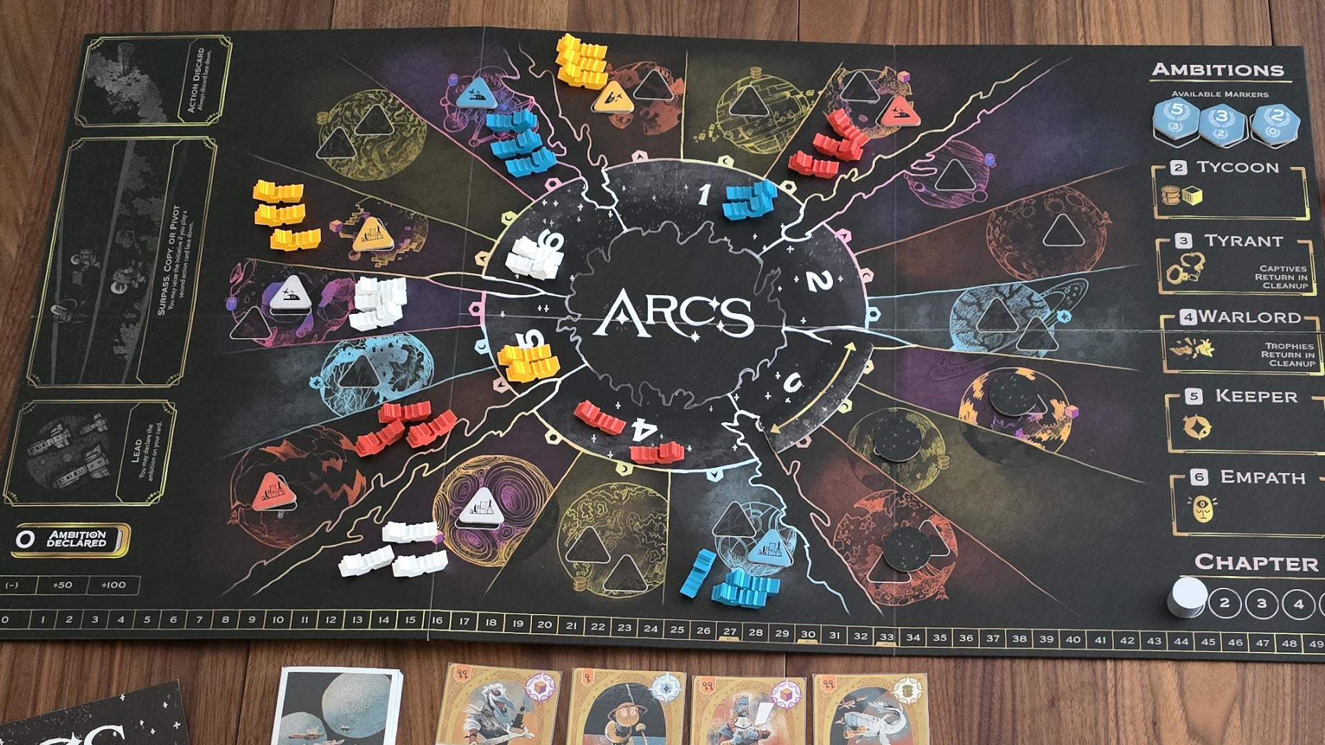 A top-down view of the Arcs board in play on a wooden table, with tokens and cards laid out