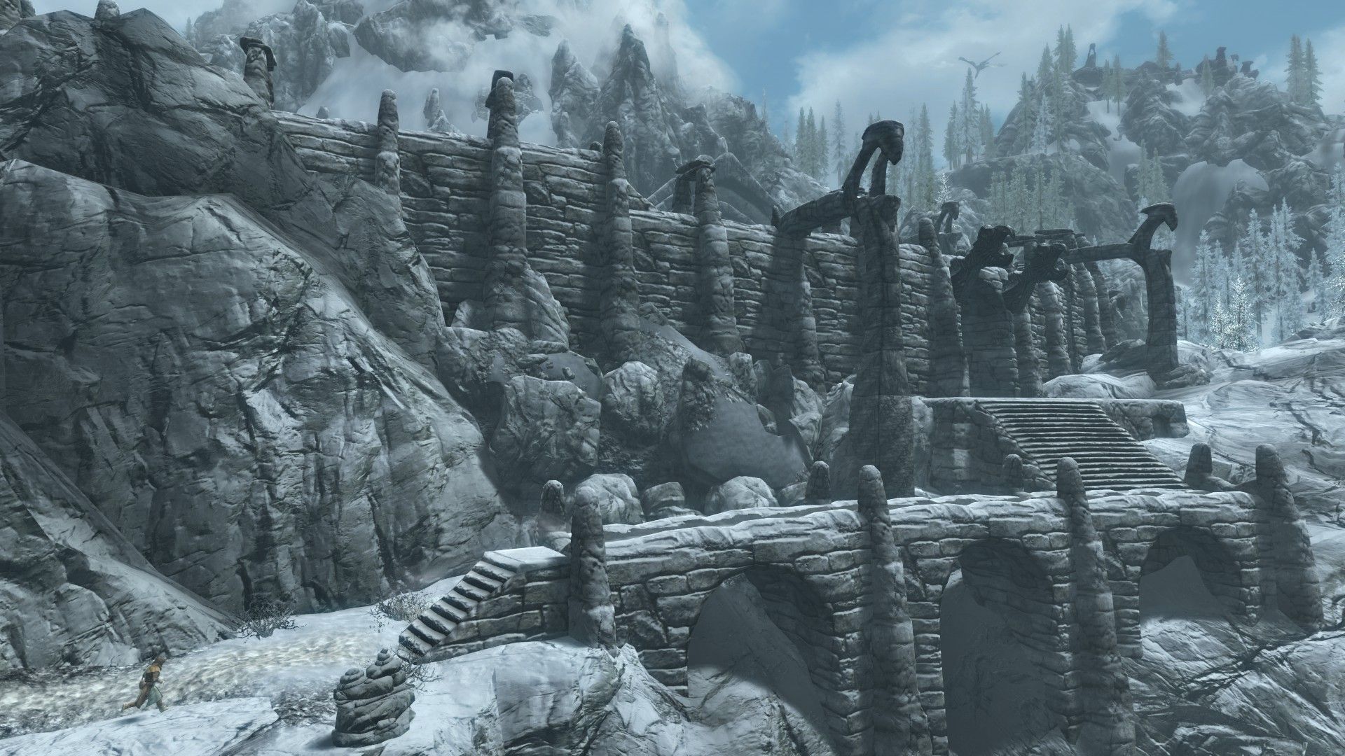 A man runs to a sprawling stone ruin in a frozen mountain in Skyrim.