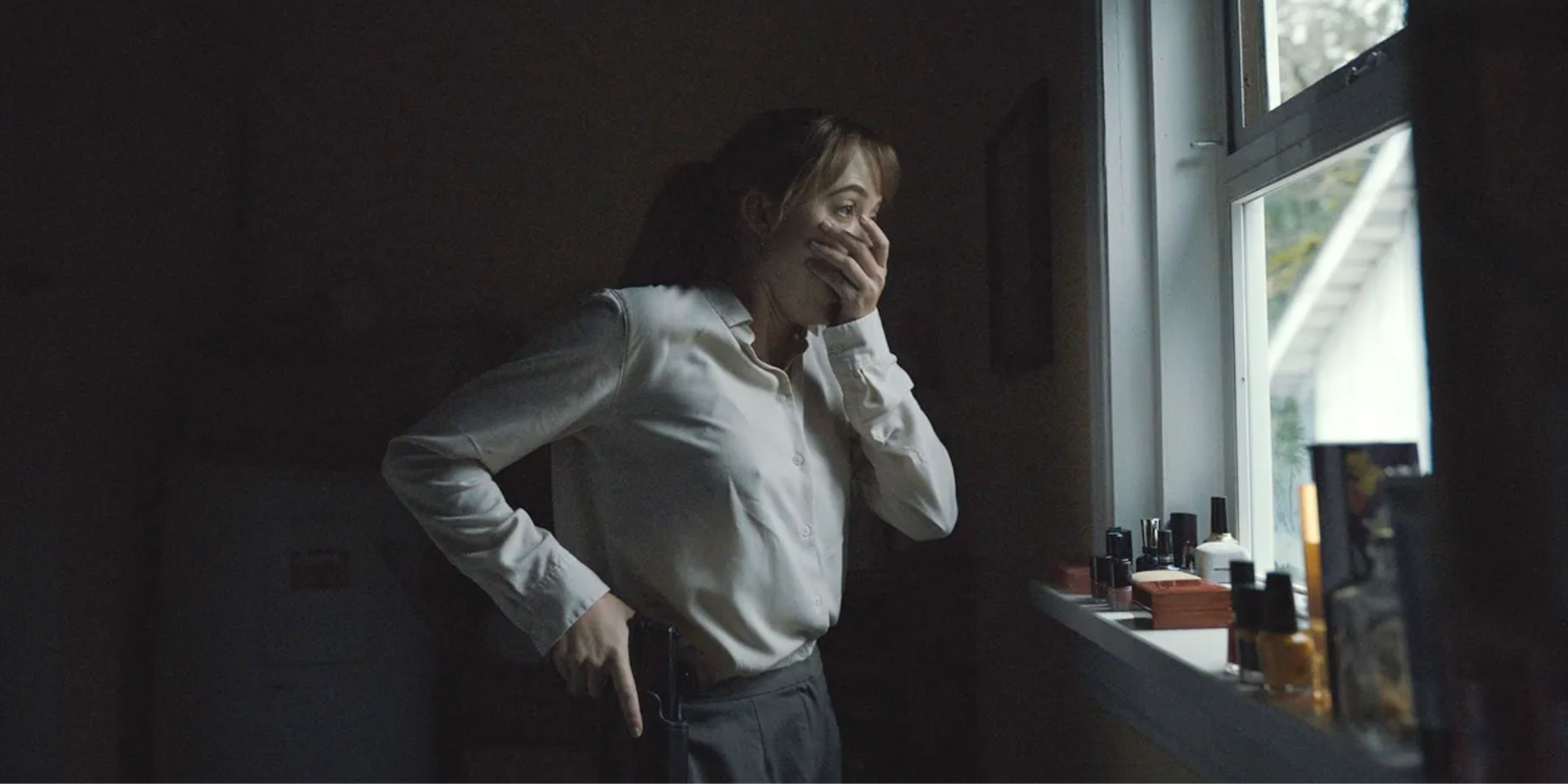 Screenshot from Longlegs movie trailer featuring a woman holding her mouth in horror as she looks out a window