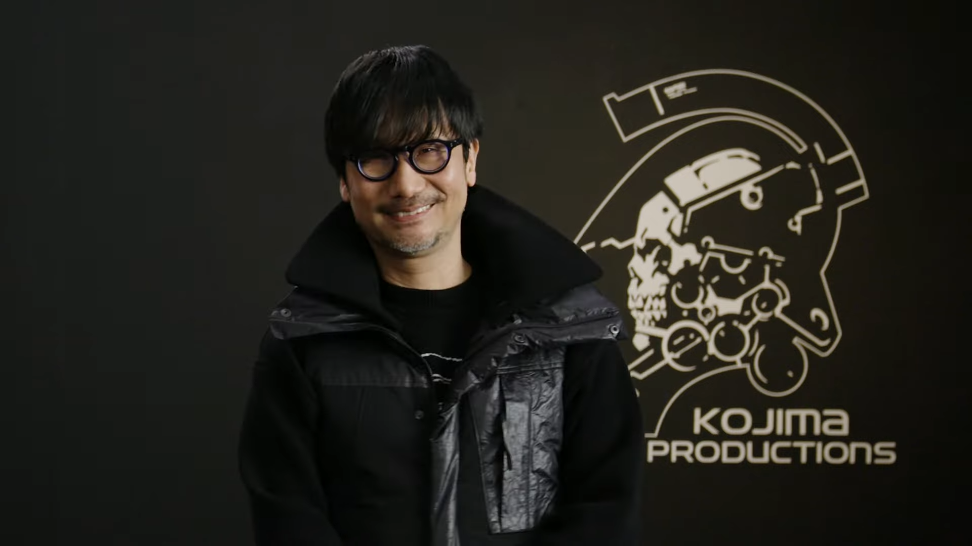 A photo showing a smiling Hideo Kojima standing in front of a Kojima Productions logo following the Physint reveal