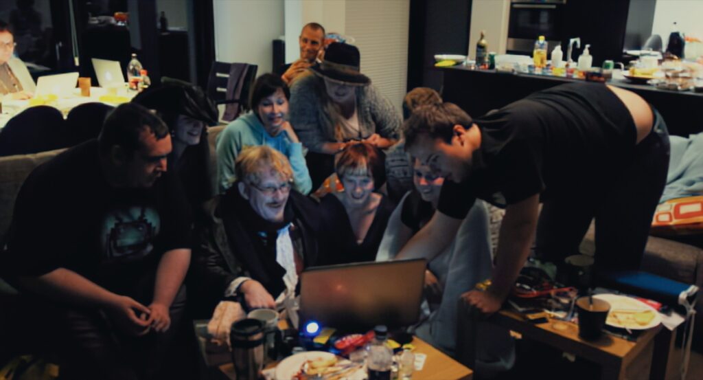 Group of people in a living room gathered around a laptop screen