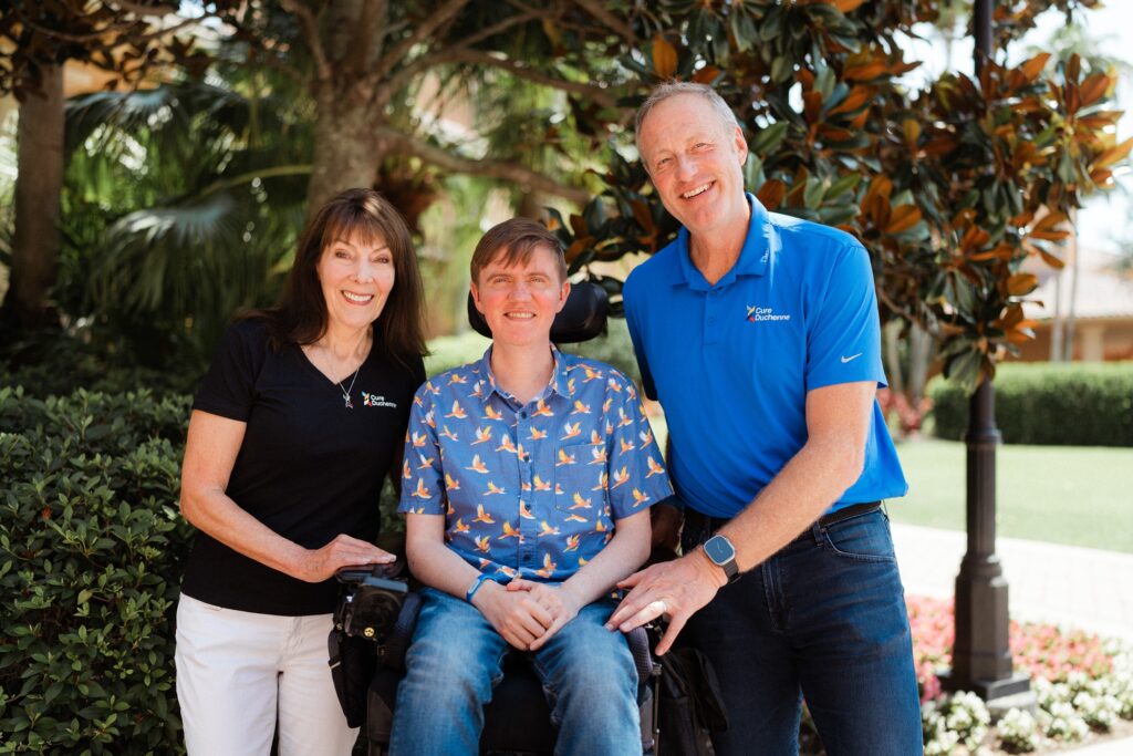 A couple flanking their adult son who's in a wheelchair, all smiling