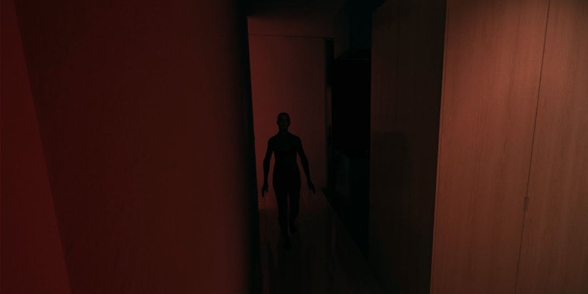 A figure menacingly approaches the viewer in a red hallway.