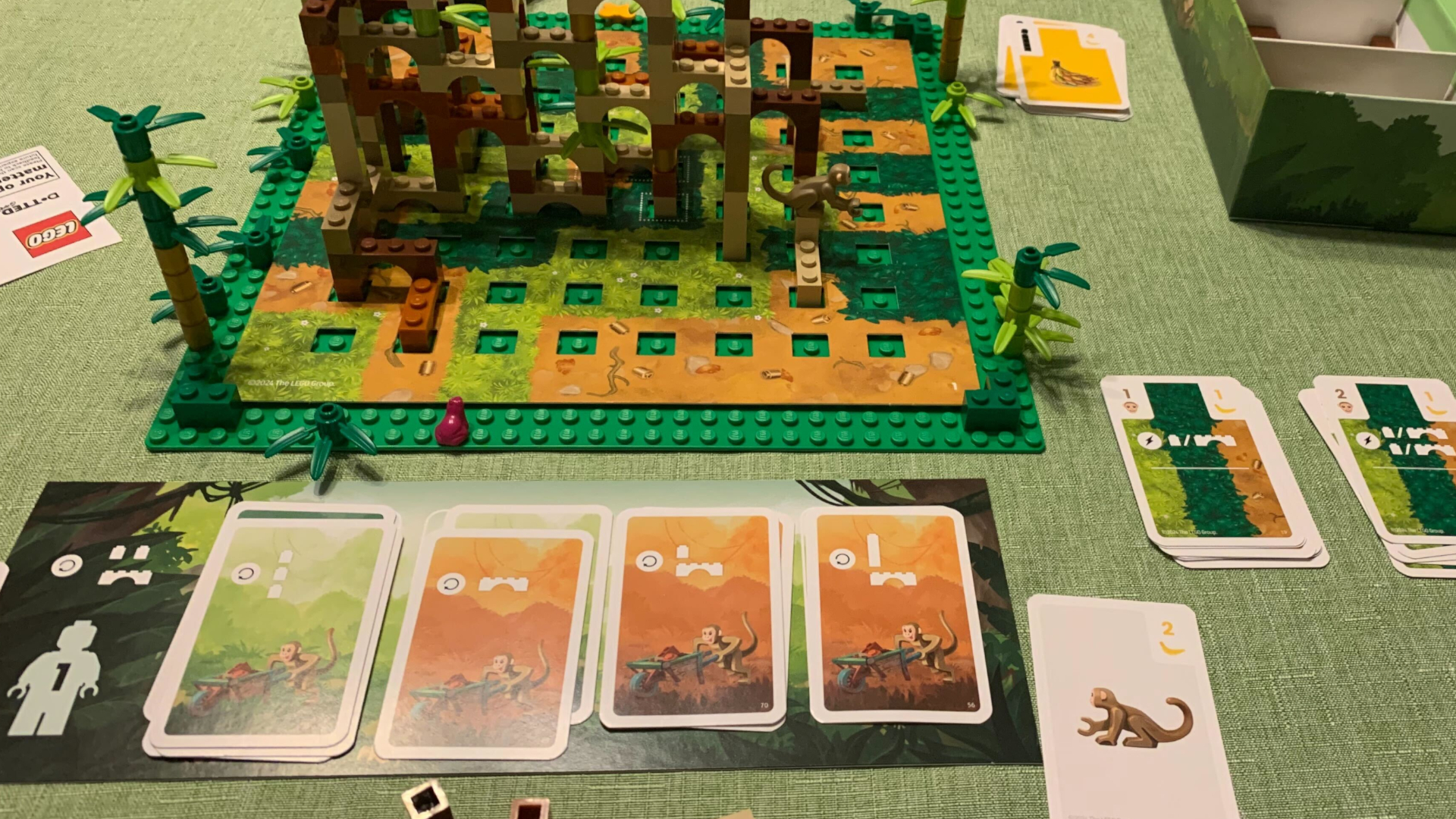 A view of the Lego Monkey Palace board, cards, and pieces laid out on a green surface