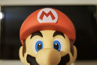 Image taken by author Rosalie Newcombe of the official Super Mario Good Smile Company Nendoroid figure sitting infront of a Nintendo Switch OLED.