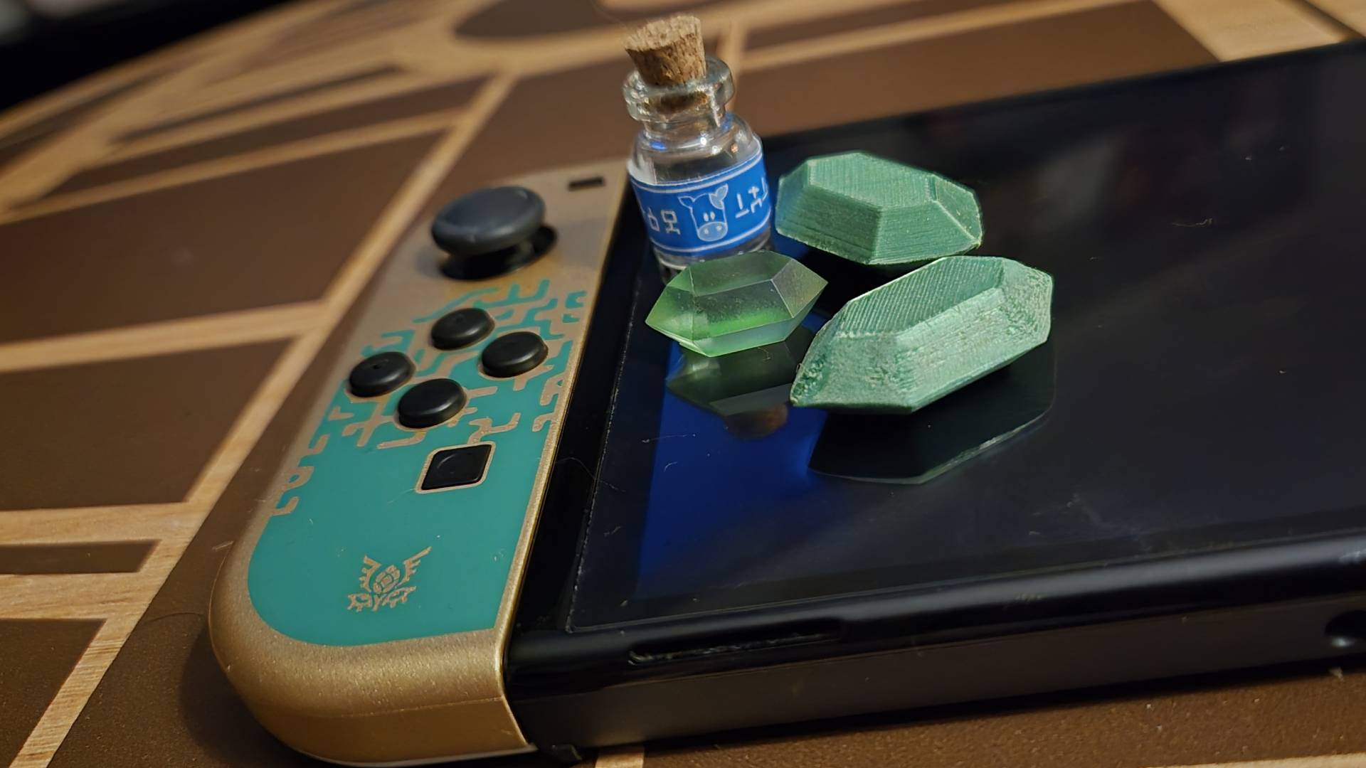 Close up of the left Joy-Con of the Tears of the Kingdom Nintendo Switch OLED model with replicas of items from the Zelda game sitting on top.