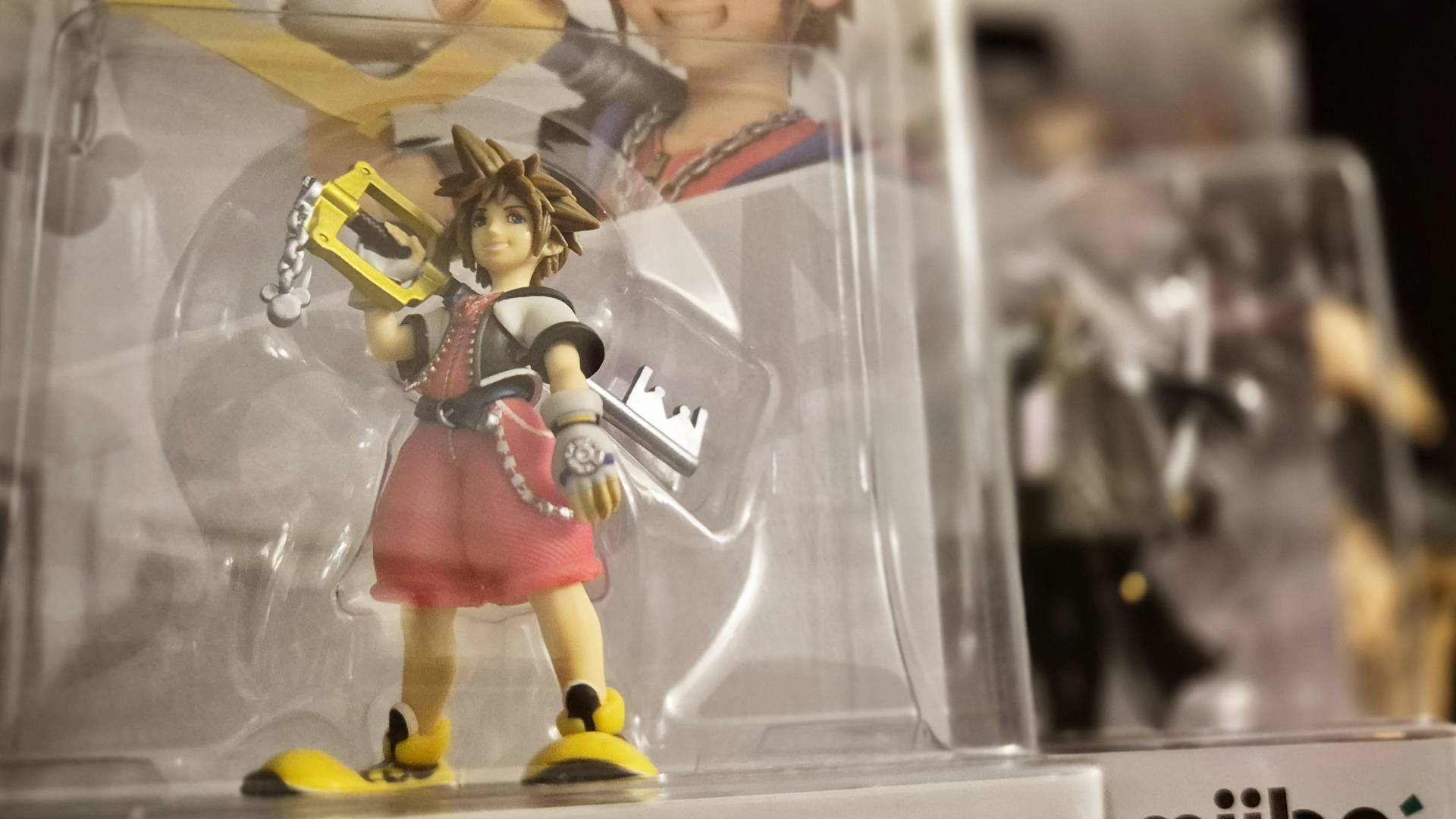 Image of the Sora Kingdom Hearts amiibo still in its box on the left, with the Sephiroth amiibo blurred in the background.