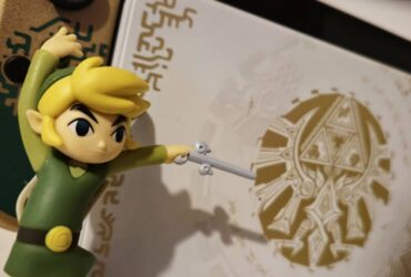 Image of the Wind Waker Link amiibo standing in front of the Tears of the Kingdom Nintendo Switch OLED.