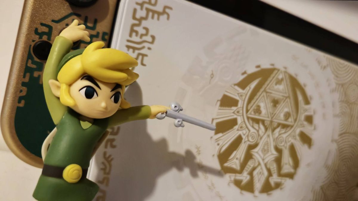 Image of the Wind Waker Link amiibo standing in front of the Tears of the Kingdom Nintendo Switch OLED.