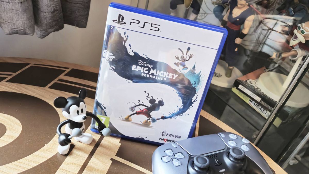 Image of the PS5 copy of Epic Mickey Rebrushed sitting on a coffee table with a Mickey toy and DualSense controller sitting infront of it.