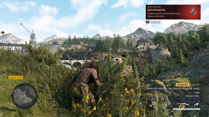 Harry crouches in the undergrowth on a sunny day in Sniper Elite Resistance. In the distance is a French chateau and a dam. In the top corner, Harry has secured a medal for 