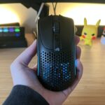 Hand holding Glorious Model O 2 Mini Wireless gaming mouse against a PC setup