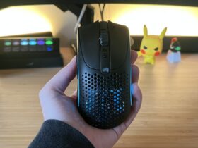 Hand holding Glorious Model O 2 Mini Wireless gaming mouse against a PC setup