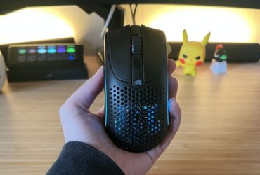 Hand holding Glorious Model O 2 Mini Wireless gaming mouse against a PC setup