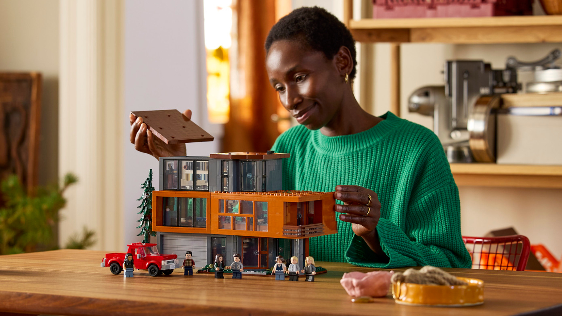 A woman sat at a wooden table puts the final roof piece on the Lego Twilight set