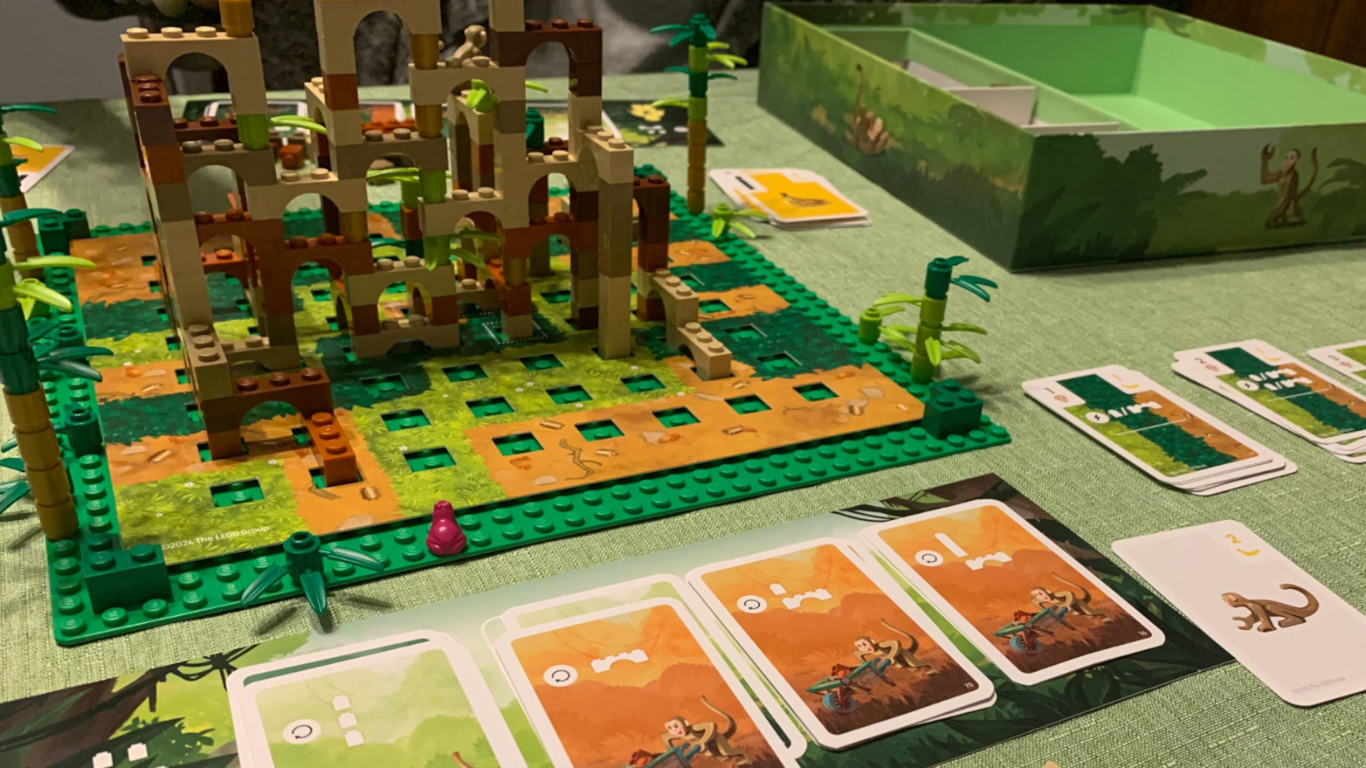 The Lego Monkey Palace board game board, pieces, and cards laid out on a green surface