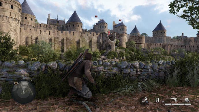 Your character, Harry, crouches behind a stone wall in the foreground in Sniper Elite Resistance. In the background, under a cloudy summer sky, sits a citadel or fort with turrets and high stone walls. A nazi banner with a swastika hangs over the entrance.