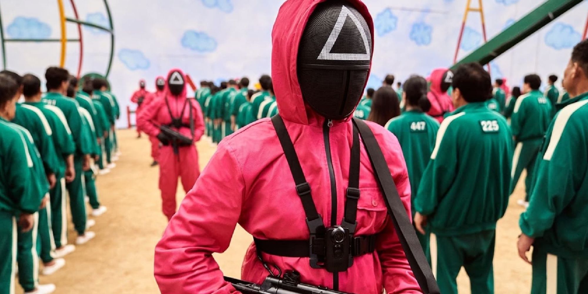 The Guards in Squid Game walking with rifles past long lines of participants in a sandy setting.